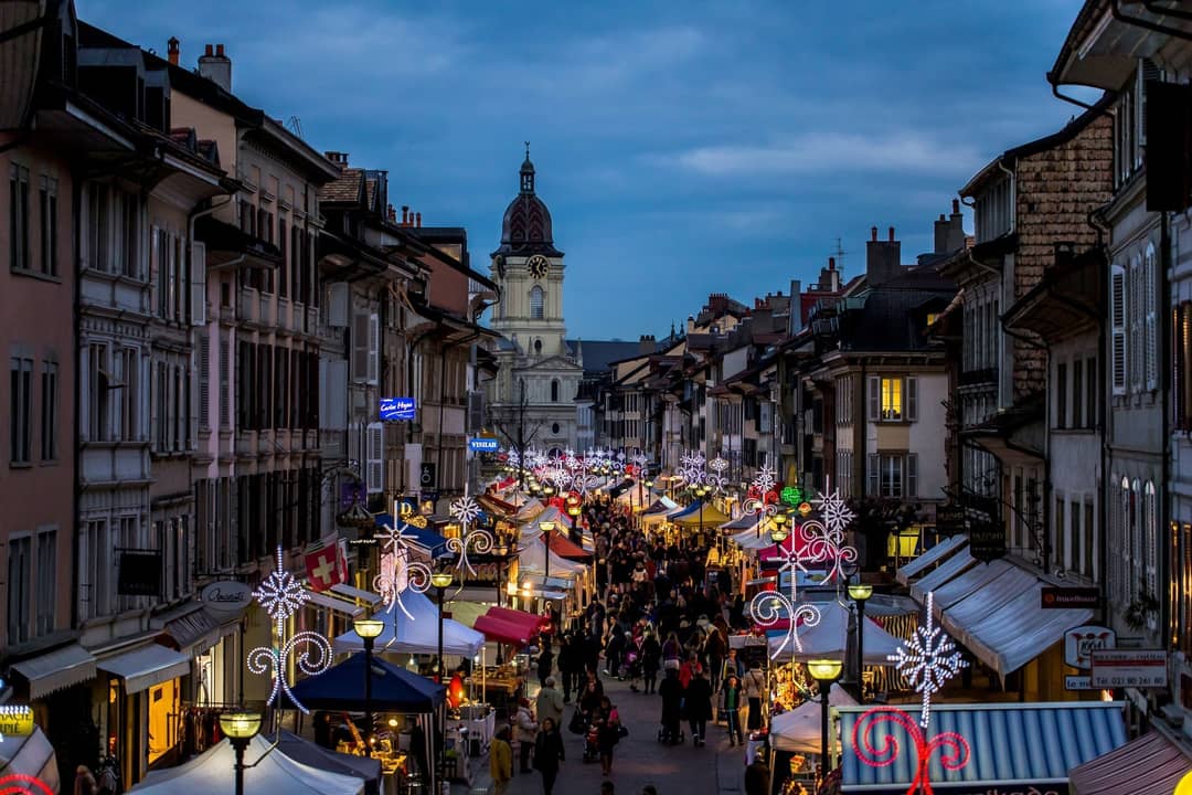 La Grand-Rue de Morges un soir de marché, les stands illuminés de part et d'autre et le Temple au fond de la rue.